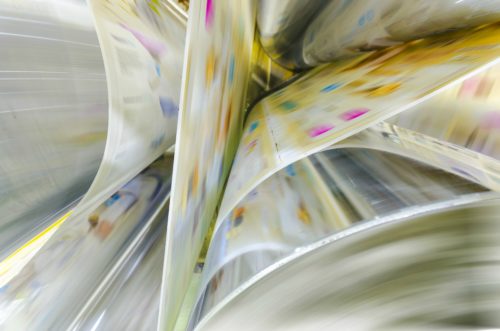 A large webset offset printing press running a long roll off paper over its rollers at high speed.