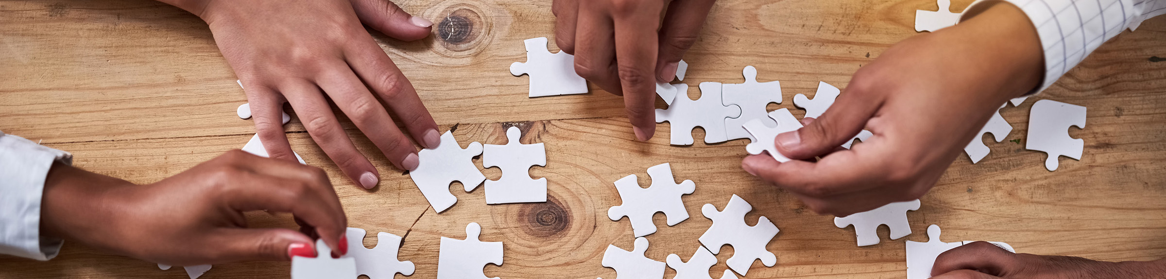 Close up of team of people arranging a jigsaw puzzle with all white pieces.