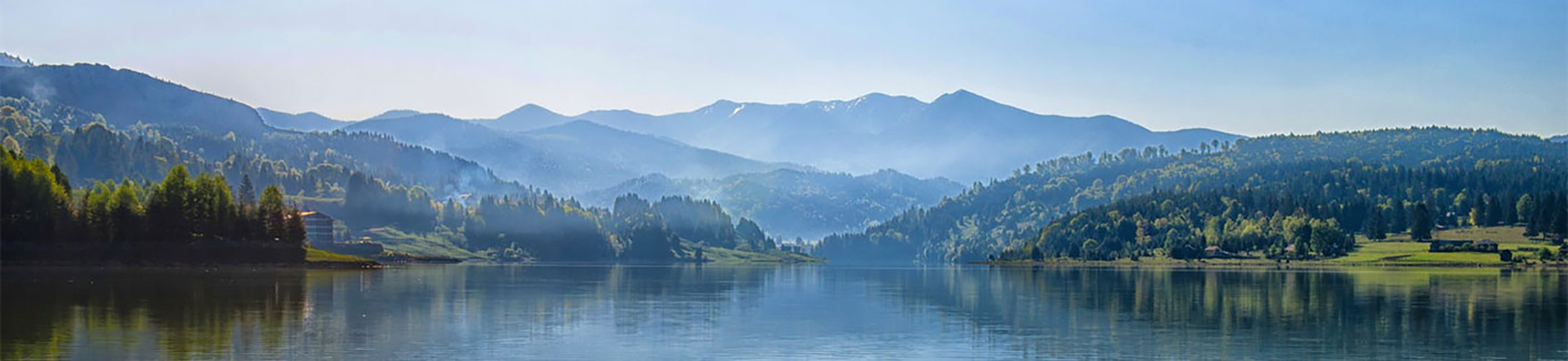 View of a quiet lake with surrounded by fir trees and misty mountains.